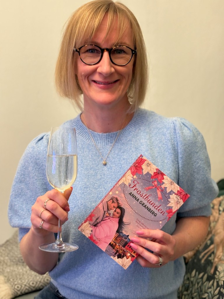 Porträtt av författaren Anna Granberg som håller ett champagneglas i handen och visar upp sin senaste roman Frostbunden.